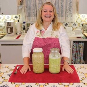 Mary in her kitchen behind a table with two jars of sauerkraut on the table.