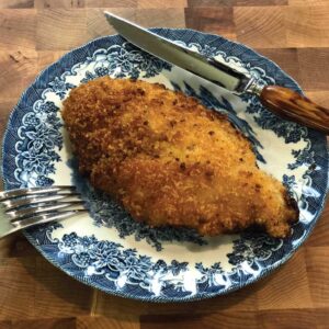 Crispy chicken cutlets on a blue and white plate with a fork and knife.