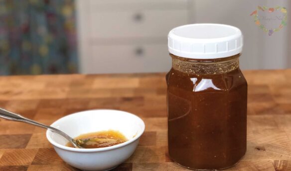 A jar of ginger honey on the table with a bowl next to it with some honey and a spoon in it.