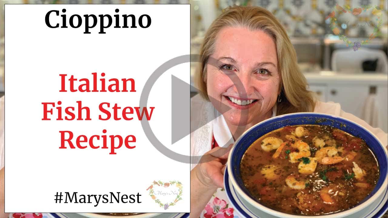 Mary holding up a bowl of Cioppino, Italian fish stew in her kitchen with text on the side part of the image.