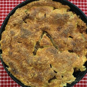 A skillet apple pie on top of a red and white checkered tablecloth.