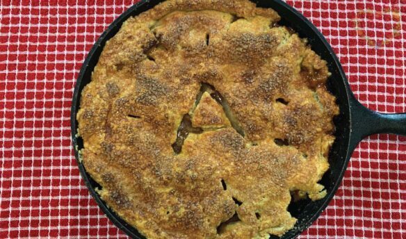 A skillet apple pie on top of a red and white checkered tablecloth.