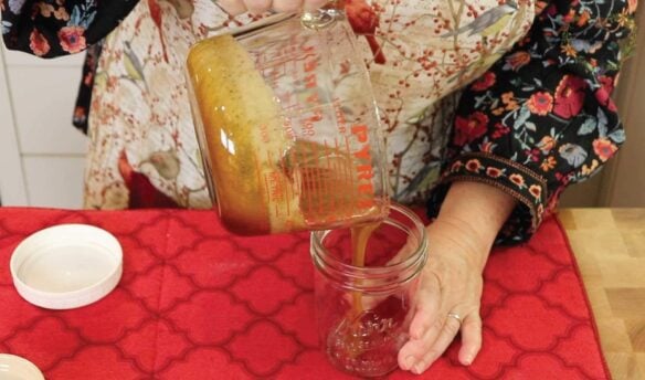 Pouring homemade cough syrup into a jar on the table.