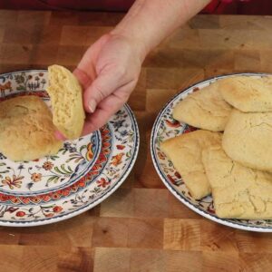 Whole wheat biscuits on a plate with hands breaking one in half on another plate to the side.